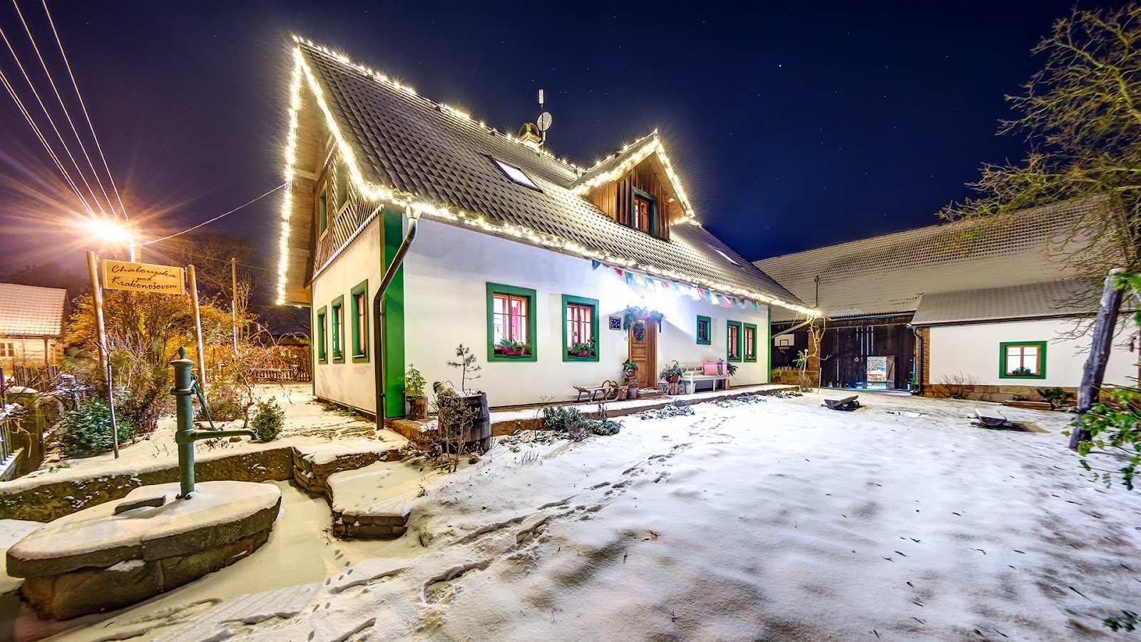 Oświetlony dom z lampkami choinkowymi na dachu i elewacji w zimowej scenerii.
